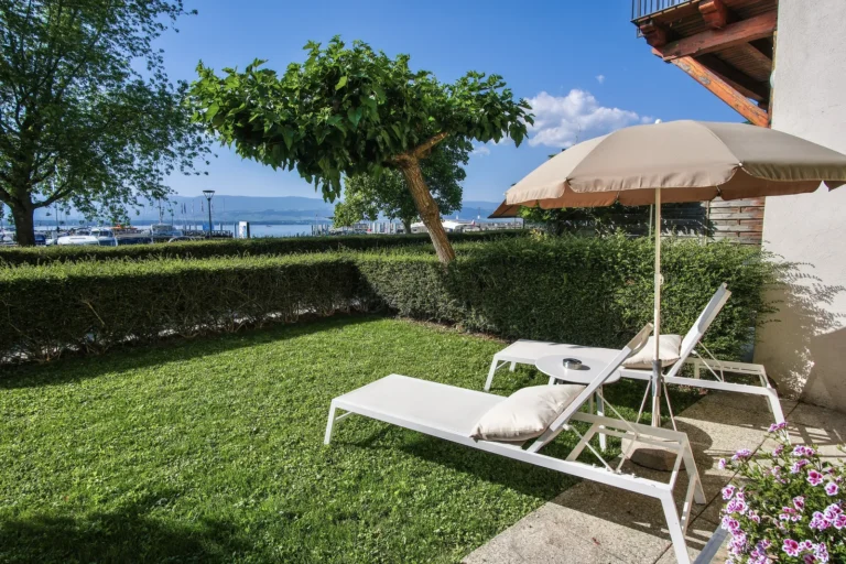 Terrasse jardin avec parasol et transat face au lac, hôtel La Riviera Victoria